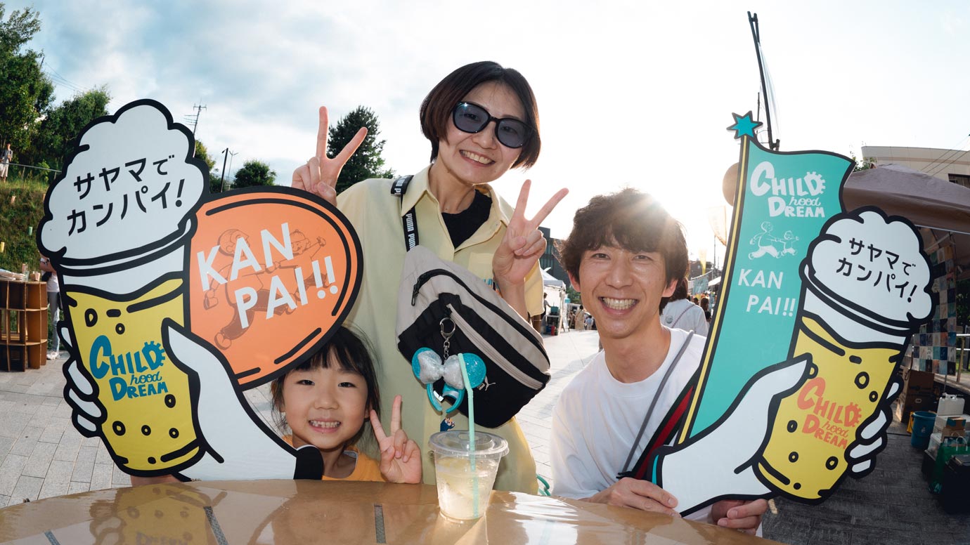 「サヤマでカンパイ!」「KAN PAI!!」と書かれたフォトプロップスを手に、笑顔で記念撮影する親子